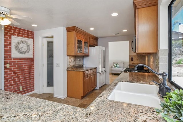 kitchen featuring a sink, a ceiling fan, tasteful backsplash, and glass insert cabinets