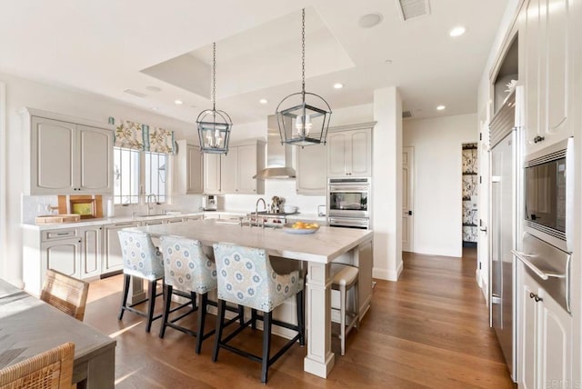 kitchen with a kitchen breakfast bar, appliances with stainless steel finishes, a center island with sink, a warming drawer, and wall chimney exhaust hood