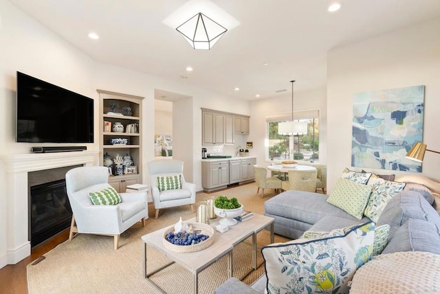 living room with recessed lighting, a glass covered fireplace, built in features, and light wood finished floors