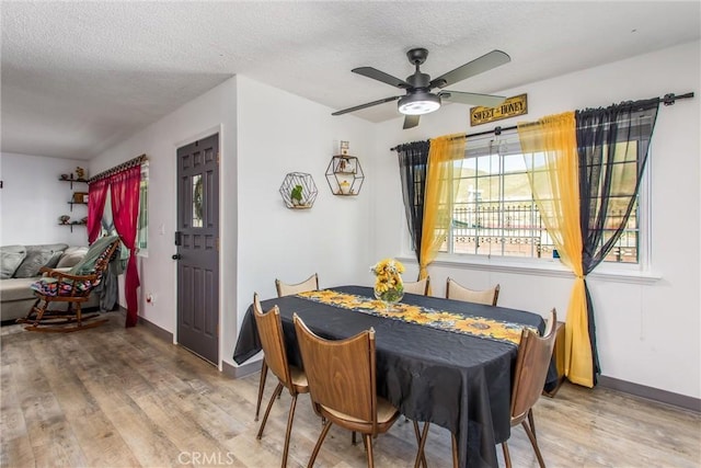 dining space featuring baseboards, a ceiling fan, a textured ceiling, and wood finished floors