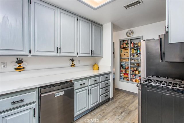 kitchen featuring appliances with stainless steel finishes, light countertops, gray cabinets, light wood-type flooring, and visible vents