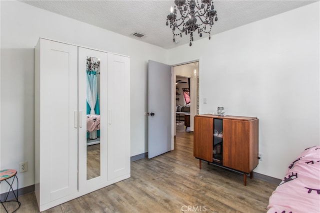 bedroom with a textured ceiling, visible vents, wood finished floors, a closet, and a chandelier