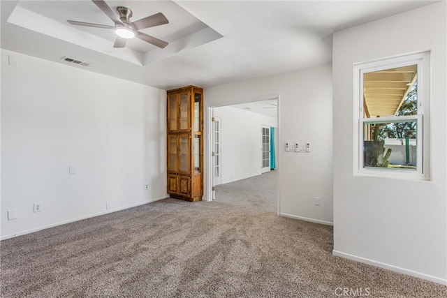 empty room with ceiling fan, visible vents, a raised ceiling, baseboards, and carpet flooring