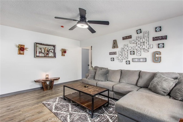 living area featuring a ceiling fan, baseboards, wood finished floors, and a textured ceiling
