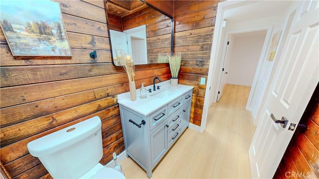 half bath with wood walls, vanity, toilet, and wood finished floors