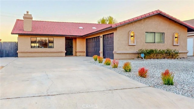 ranch-style home featuring a garage, a chimney, concrete driveway, and a tiled roof