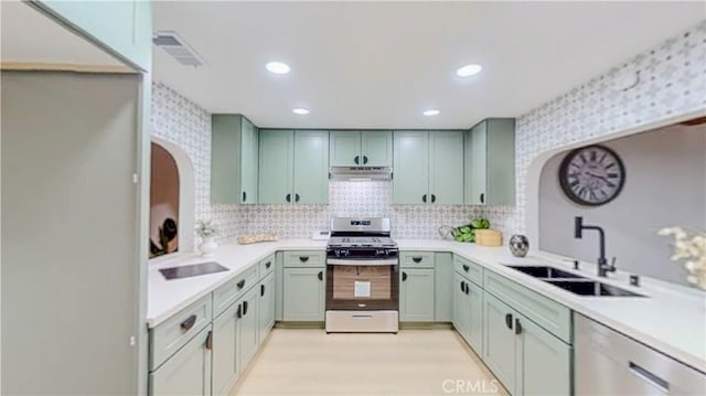kitchen with stainless steel appliances, a sink, under cabinet range hood, arched walkways, and light countertops