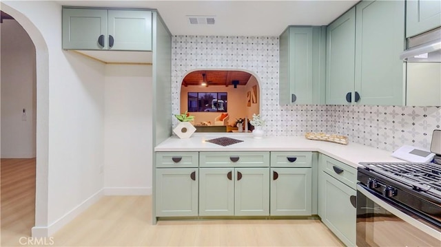 kitchen featuring stainless steel gas range oven, green cabinets, arched walkways, baseboards, and light countertops