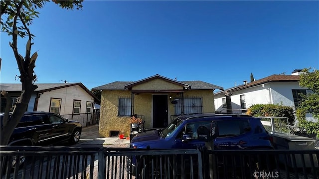 bungalow featuring fence and stucco siding