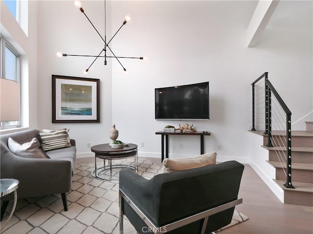living area featuring stairs, a towering ceiling, baseboards, light wood finished floors, and a notable chandelier