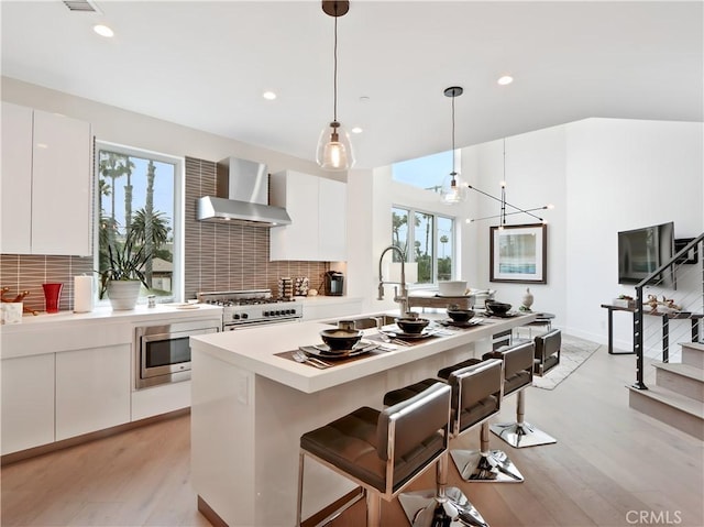 kitchen featuring a healthy amount of sunlight, stainless steel microwave, wall chimney exhaust hood, and a sink