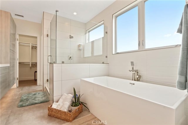 bathroom with a walk in closet, tile walls, a shower stall, visible vents, and a soaking tub