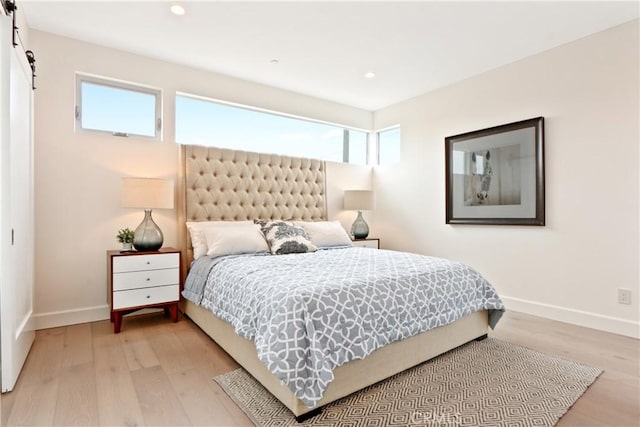 bedroom with recessed lighting, baseboards, light wood-type flooring, and a barn door