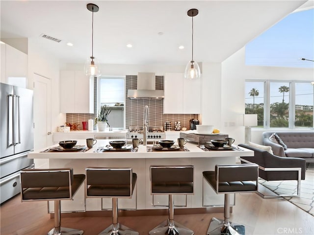kitchen featuring visible vents, modern cabinets, wall chimney range hood, and high quality fridge