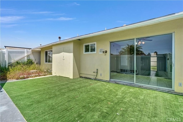 rear view of property featuring a lawn, fence, and stucco siding