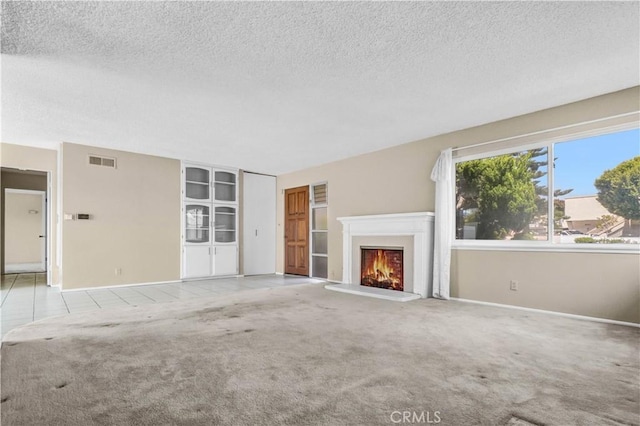 unfurnished living room featuring carpet floors, a textured ceiling, and visible vents