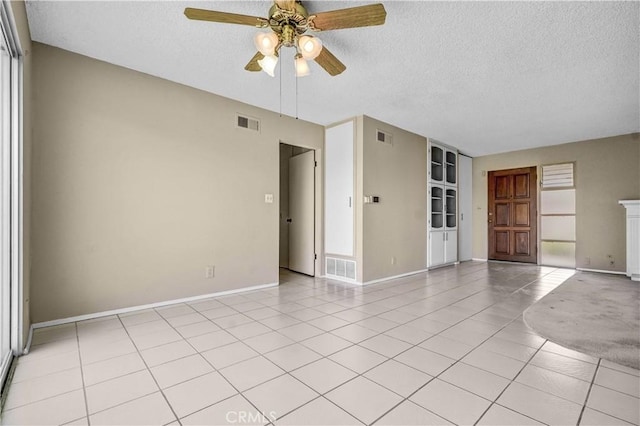 empty room with a ceiling fan, a textured ceiling, visible vents, and light tile patterned floors