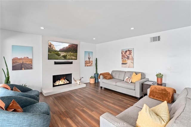 living room featuring visible vents, recessed lighting, wood finished floors, and a warm lit fireplace