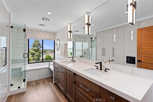 full bath featuring visible vents, a sink, wood finished floors, and a shower stall