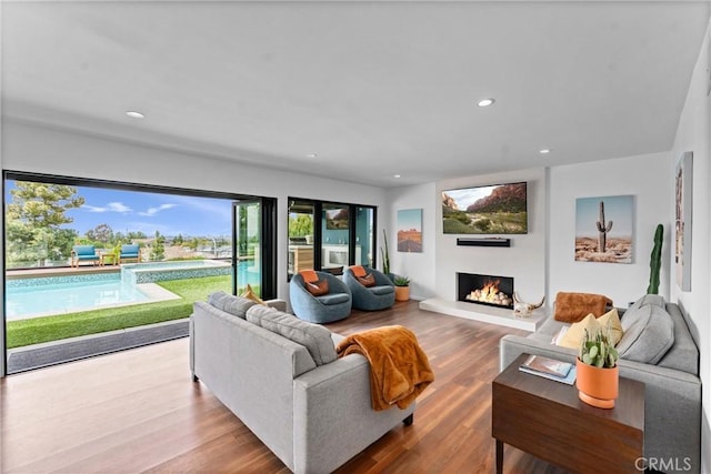 living room with recessed lighting, a lit fireplace, and wood finished floors