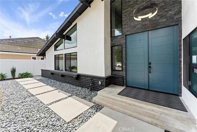 doorway to property featuring fence, stone siding, and stucco siding
