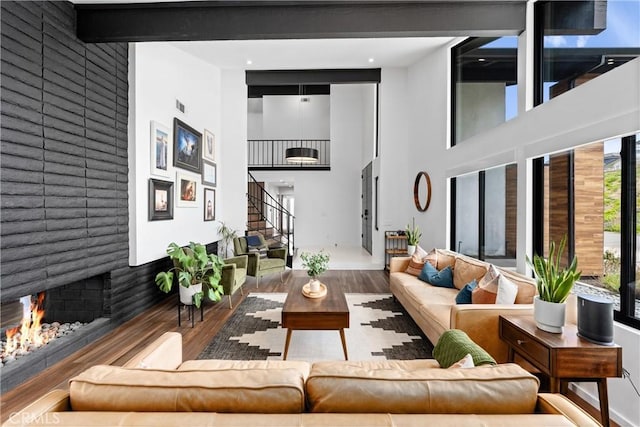 living room with a lit fireplace, visible vents, a towering ceiling, wood finished floors, and stairs