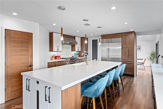 kitchen featuring dark wood-style flooring, visible vents, high end appliances, a spacious island, and a sink