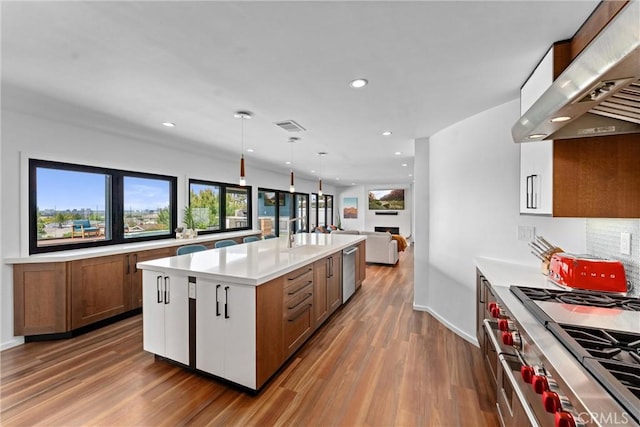 kitchen with light countertops, stainless steel appliances, wood finished floors, under cabinet range hood, and visible vents