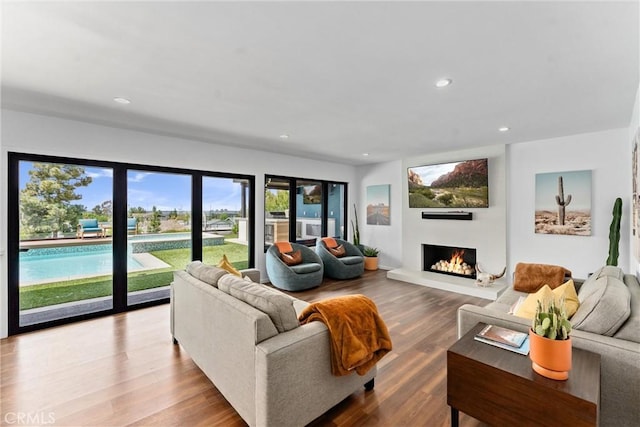 living area featuring recessed lighting, a lit fireplace, and wood finished floors