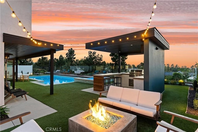 view of swimming pool featuring a lawn, an outdoor living space with a fire pit, a fenced backyard, and a bar