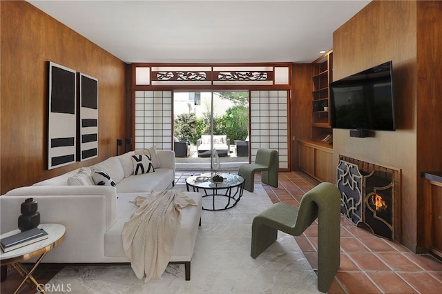 living room with light tile patterned floors, wood walls, and a warm lit fireplace