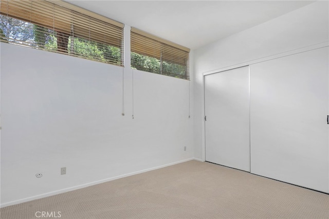 unfurnished bedroom with baseboards, a closet, and light colored carpet