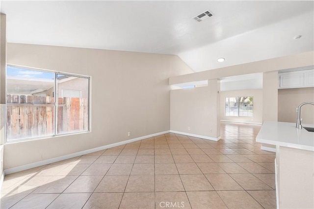 unfurnished living room featuring visible vents, baseboards, a sink, light tile patterned floors, and vaulted ceiling