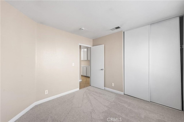 unfurnished bedroom featuring a closet, baseboards, light colored carpet, and visible vents