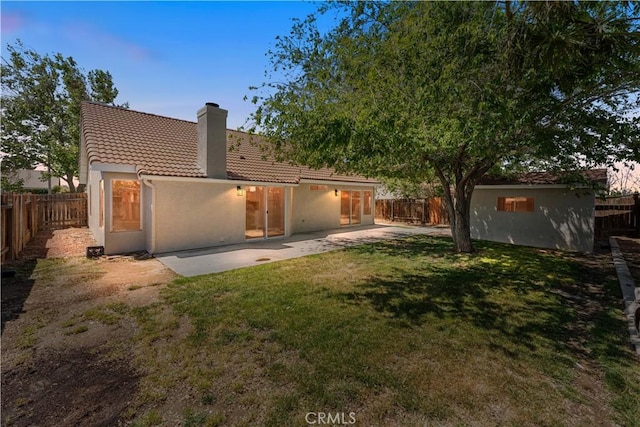 rear view of property featuring a yard, a chimney, stucco siding, and a tile roof