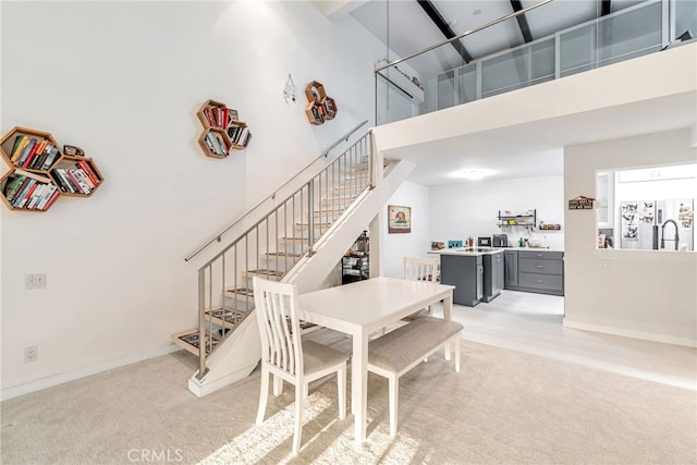 dining area with baseboards, light carpet, stairs, and a towering ceiling