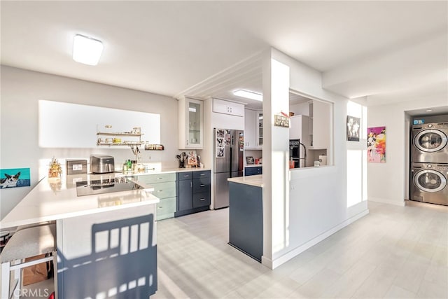 kitchen with stacked washing maching and dryer, light countertops, white cabinets, freestanding refrigerator, and glass insert cabinets