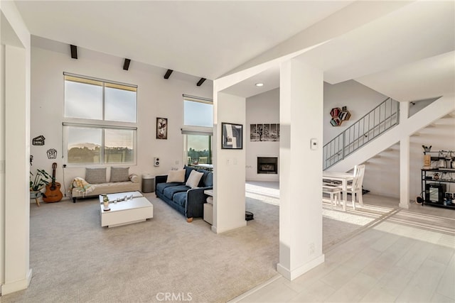 carpeted living area featuring a fireplace, baseboards, stairs, and a towering ceiling