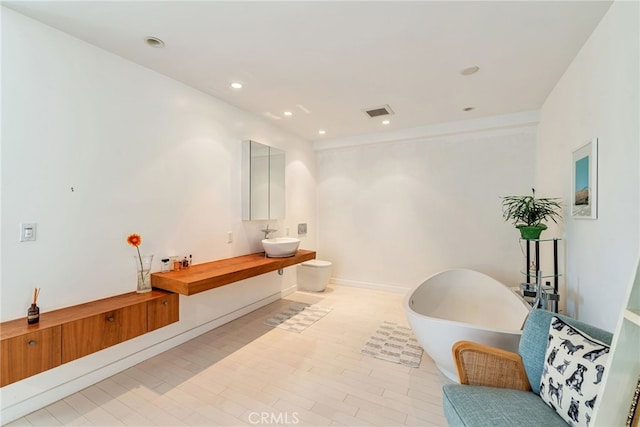bathroom featuring visible vents, a freestanding tub, wood finished floors, vanity, and recessed lighting