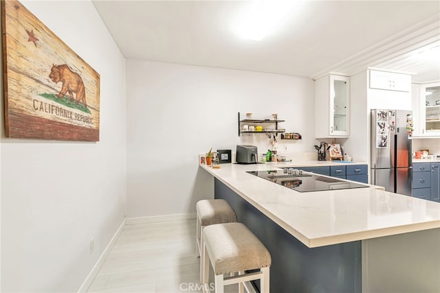 kitchen with black electric cooktop, freestanding refrigerator, a peninsula, baseboards, and a kitchen bar