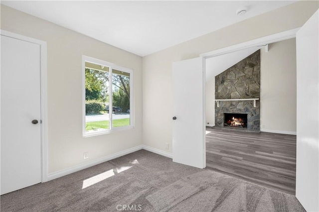 unfurnished living room with baseboards, carpet flooring, and a stone fireplace