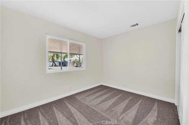 empty room with baseboards, dark colored carpet, and visible vents
