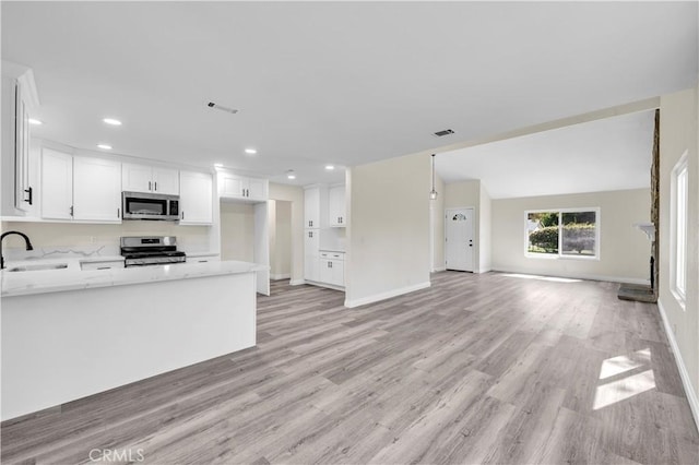 kitchen featuring a sink, light stone counters, white cabinets, open floor plan, and stainless steel appliances