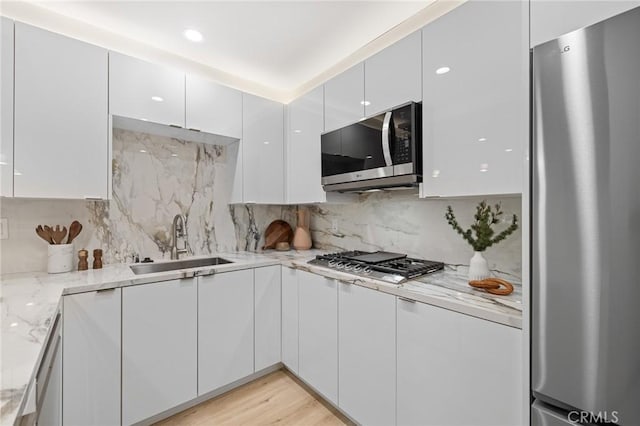kitchen featuring white cabinets, light stone countertops, appliances with stainless steel finishes, a sink, and modern cabinets