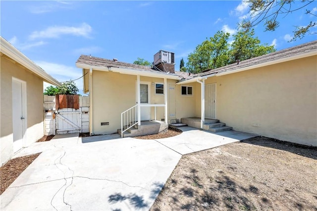 back of house with a chimney, central AC unit, a gate, a patio, and stucco siding