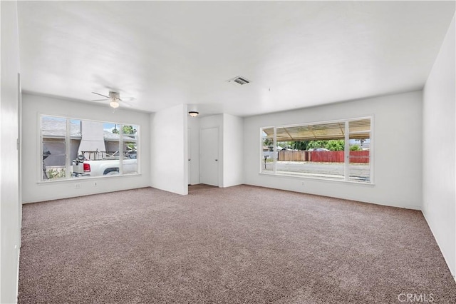 unfurnished living room with carpet floors, ceiling fan, visible vents, and plenty of natural light