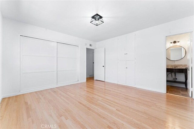 unfurnished bedroom with visible vents, baseboards, a closet, light wood finished floors, and ensuite bathroom