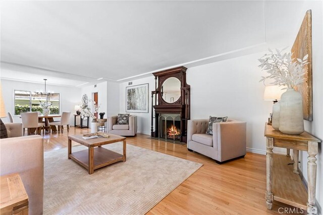 living area featuring light wood-type flooring, baseboards, a notable chandelier, and a large fireplace