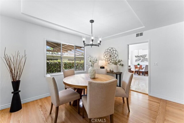 dining space with an inviting chandelier, a raised ceiling, light wood finished floors, and visible vents