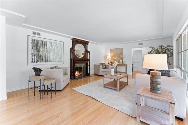 living room with visible vents, a fireplace with flush hearth, baseboards, and wood finished floors
